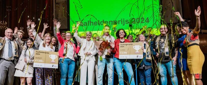 Winnaars van de taalheldenprijs juichen op een podium